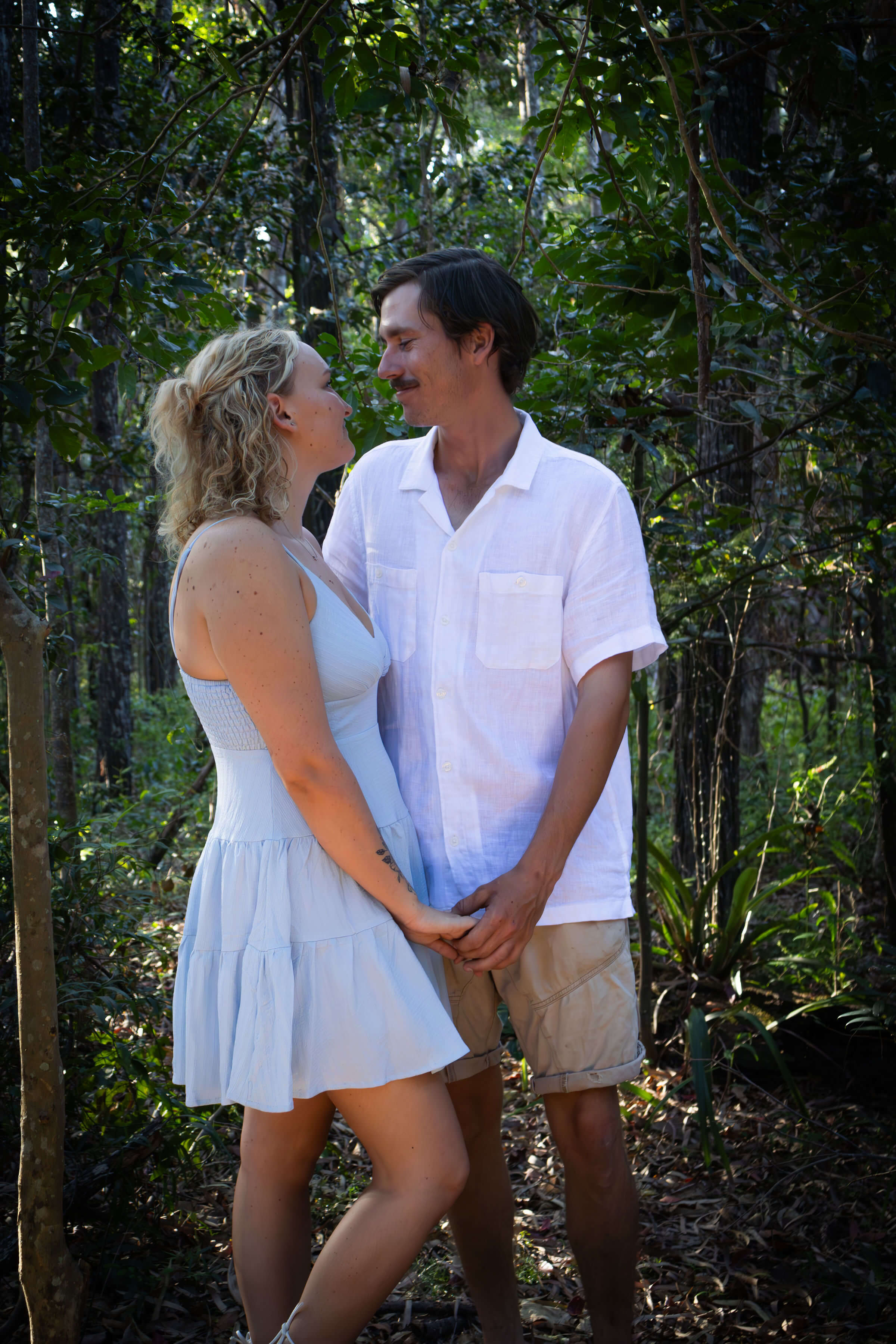 a loving couple looking into each others eyes with the forest behind them