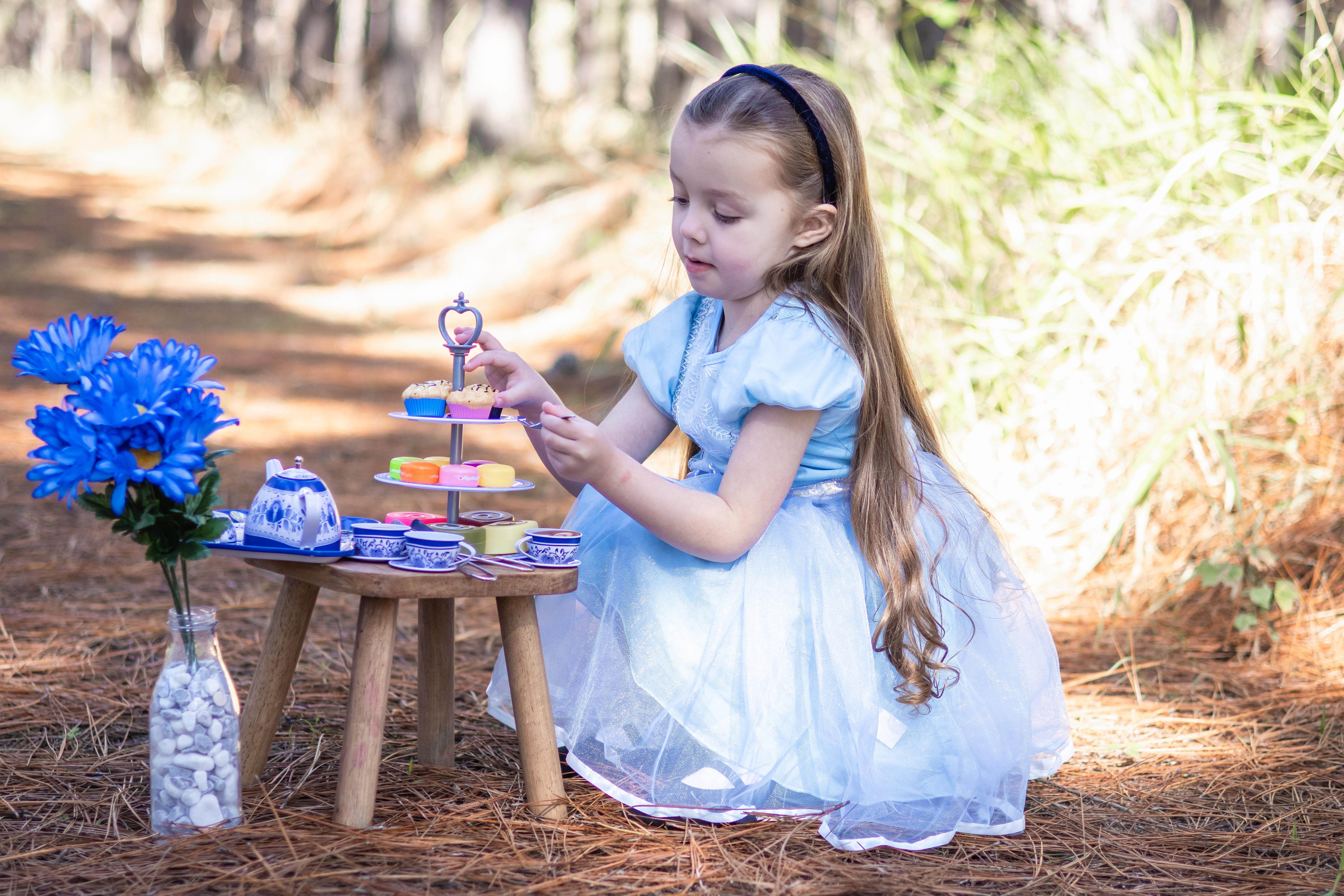 a young girl dressed as Alice from wonderland having a tea party